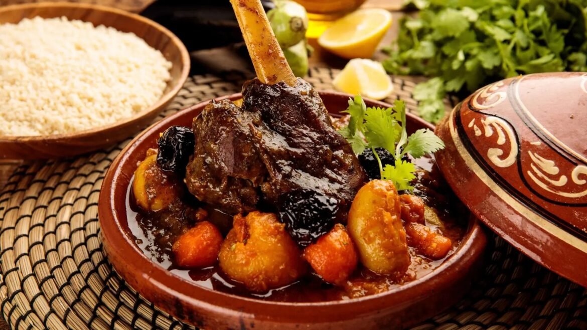 Lamb tagine with vegetables and prunes in a clay pot, garnished with cilantro, set on a woven placemat with couscous in the background
