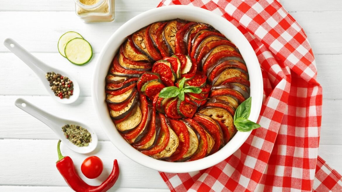 Ratatouille-style dish with neatly arranged zucchini and eggplant slices in a white bowl, topped with fresh basil.