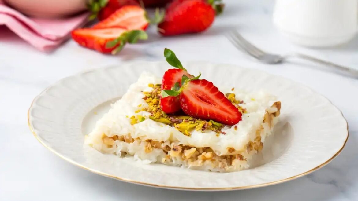 Plate with a small layered dessert topped with coconut cream, crushed pistachios, and a strawberry half garnish.