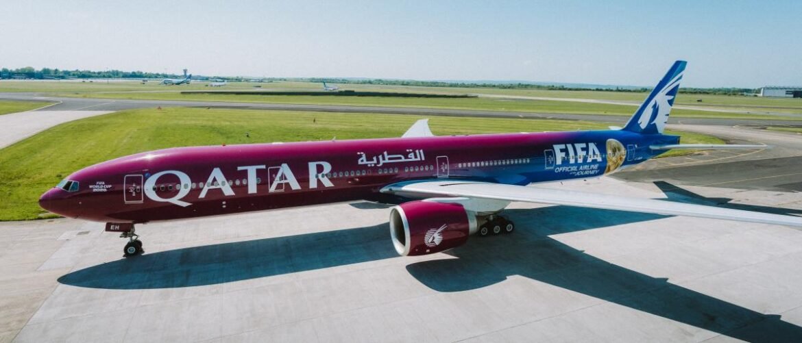 Qatar Airways plane with FIFA World Cup livery on a taxiway, maroon fuselage and blue tail winged emblem visible