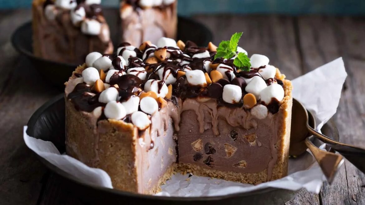 Slice of chocolate ice cream cake topped with marshmallows, nuts, and chocolate drizzle on a rustic plate with a mint garnish.