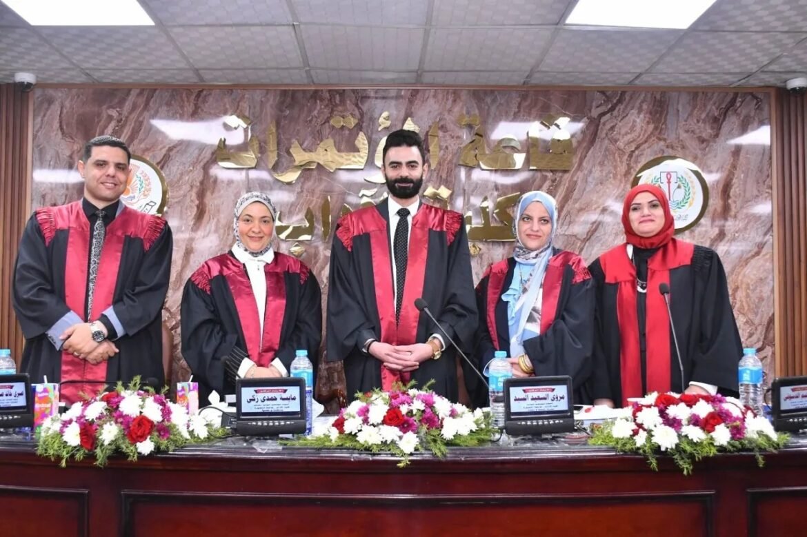 Five graduates in black gowns with red panels stand behind a decorated front table during a formal ceremony, with gold Arabic lettering on a marble wall backdrop behind them.