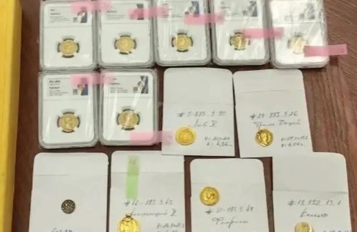 Assortment of gold coins in clear plastic holders on a wooden table, with labels and pink tape seals visible