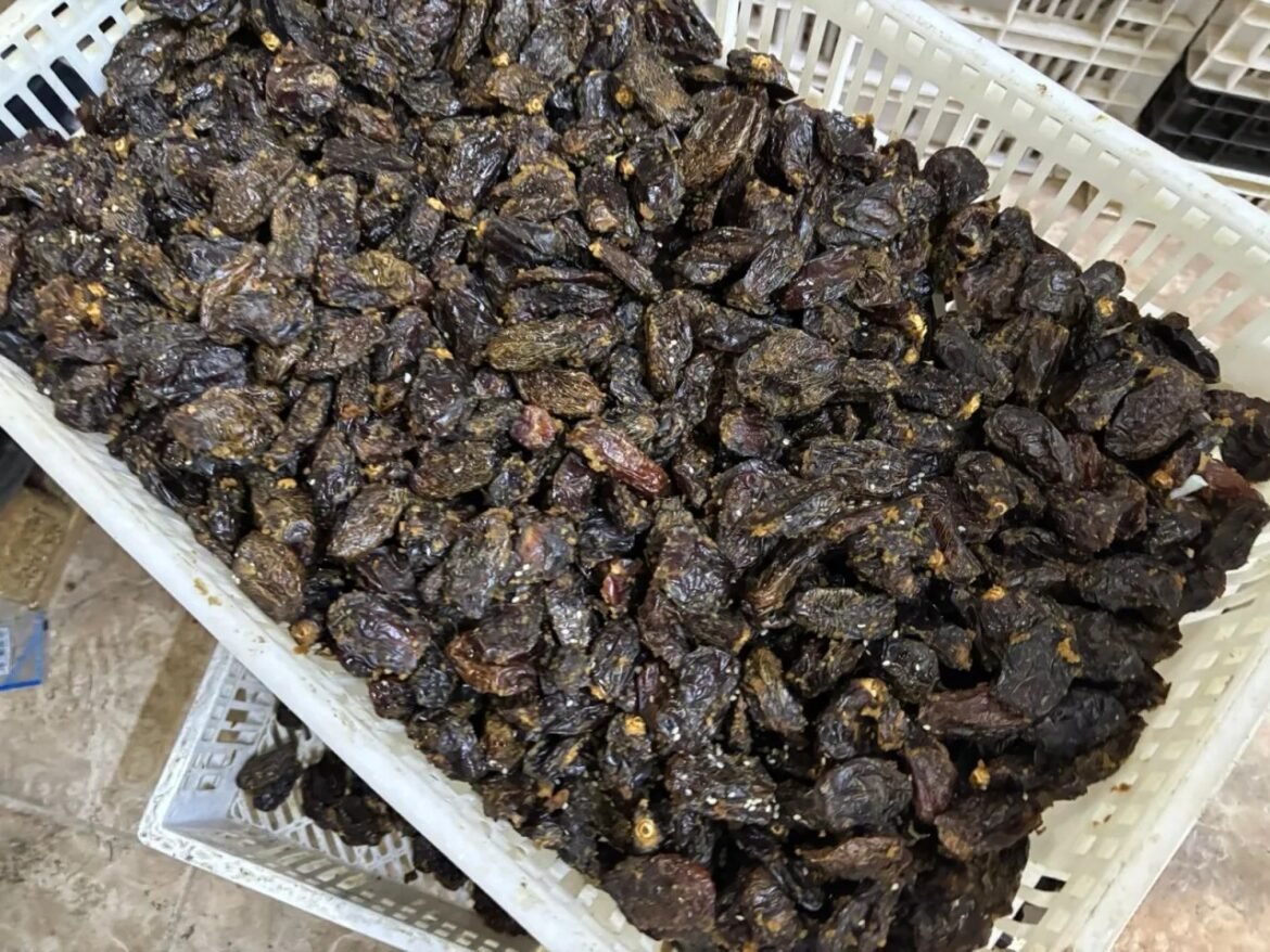 Pile of dark dried raisins in a white plastic crate at a market or warehouse setting.