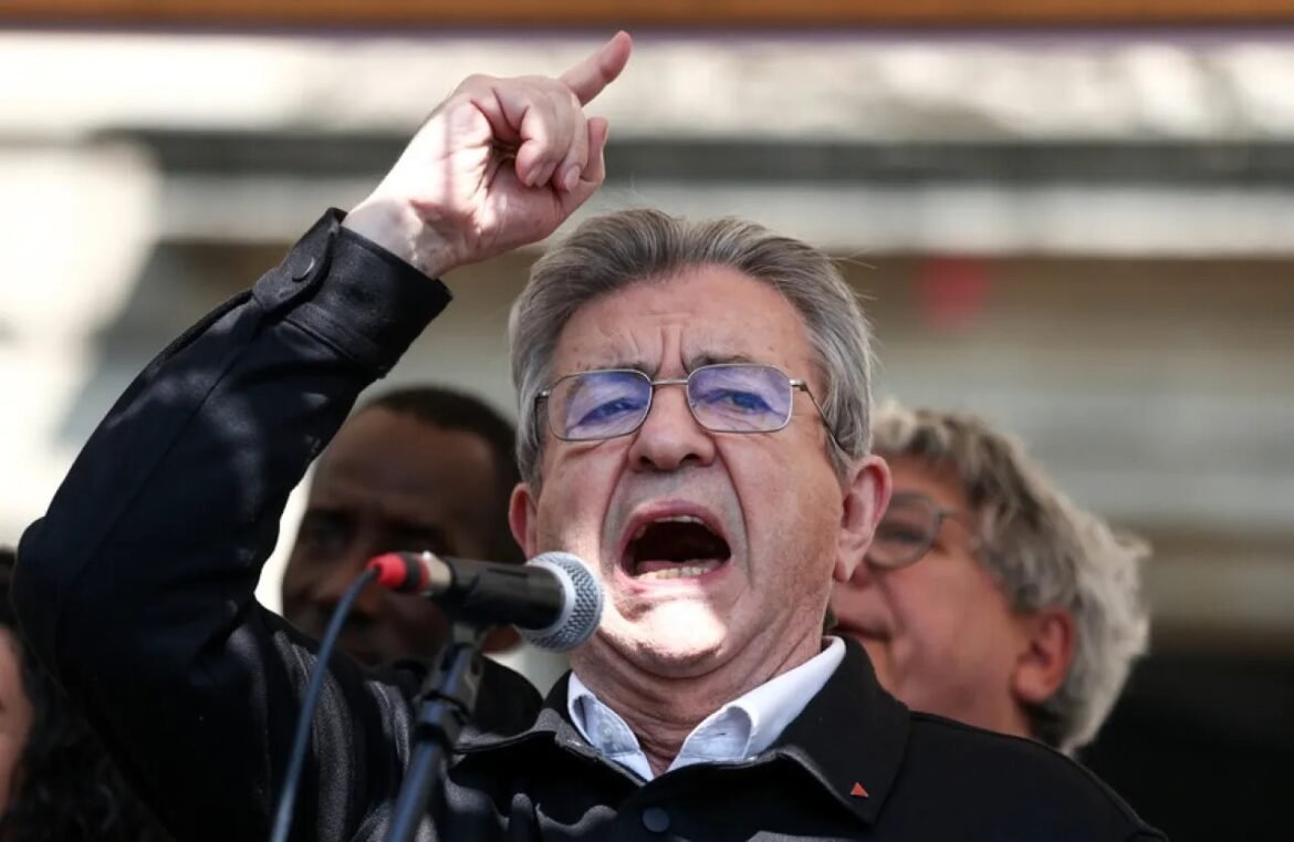 Man shouting into a microphone while raising his fist in a passionate speech at a rally, with others in the background.