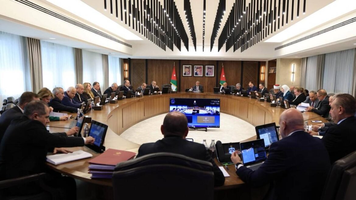 Diplomatic meeting around a large oval table with officials, laptops open and flags on the wall behind them.