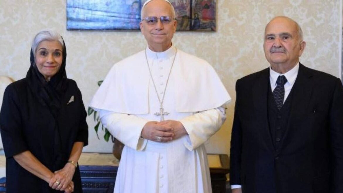 Three people stand indoors: a woman in black with a headscarf on the left, a pope in white robes and cross in the center, and a man in a dark suit on the right.
