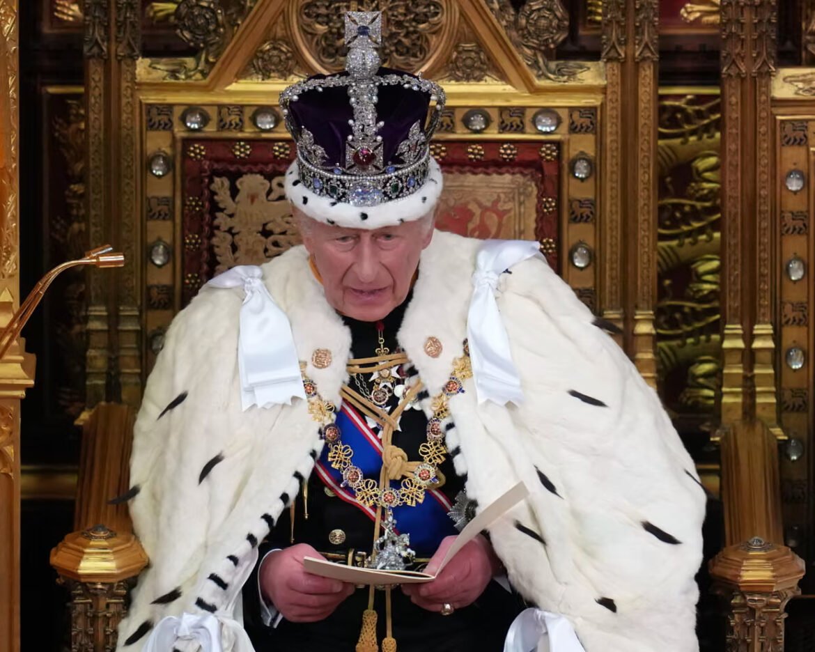 Royal figure in jewel-encrusted crown and white fur robe seated on an ornate throne, reading a document.