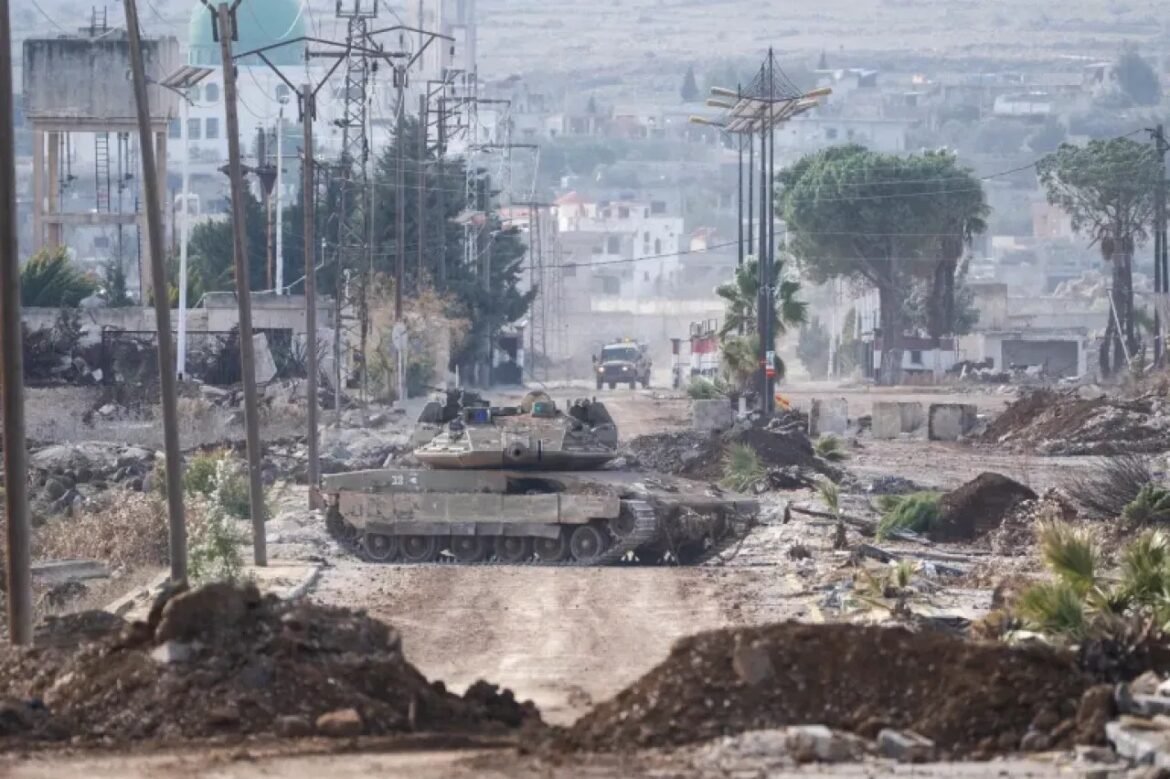 Two tanks move down a rubble-strewn urban street, with damaged buildings and debris around them.
