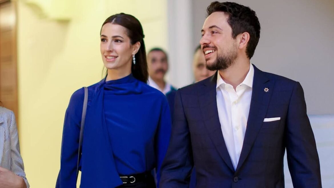 Smiling man in a navy suit and white shirt walking beside a woman in a blue blouse indoors.