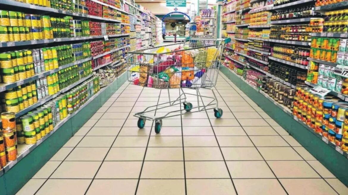 Wheeled shopping cart filled with groceries sits in a supermarket aisle between shelves.