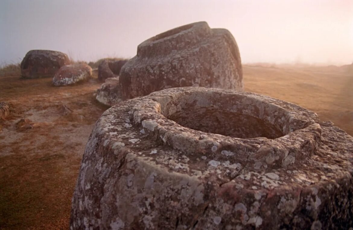 Circular stone well or altar made of weathered rocks on a grassy hill at sunrise with mist in the background