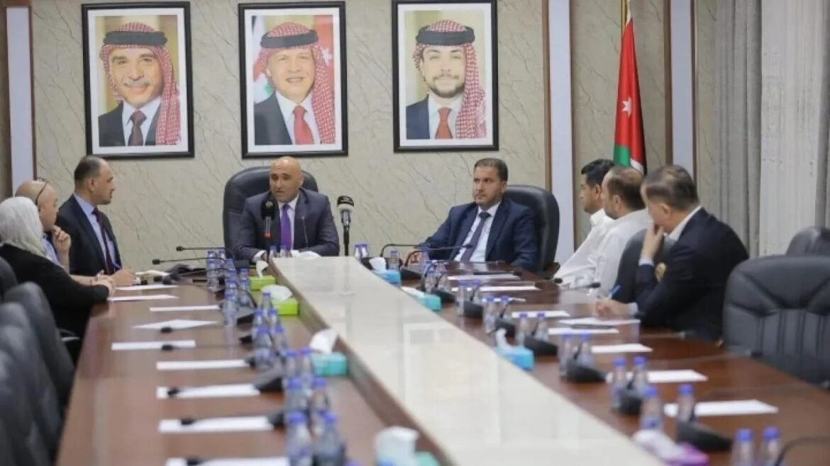 Officials seated around a long conference table in a formal meeting room, with framed portraits and a Jordanian flag in the background.