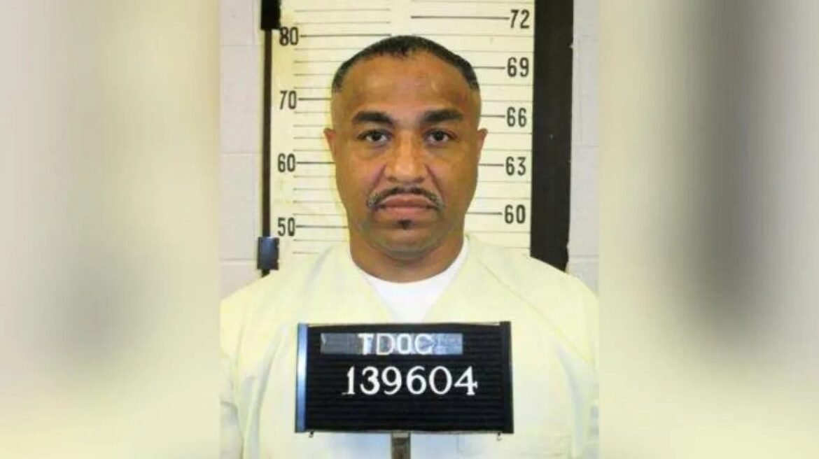 Mugshot of a man in a light jumpsuit standing before a height chart, badge showing TDOC 139604 at chest height.