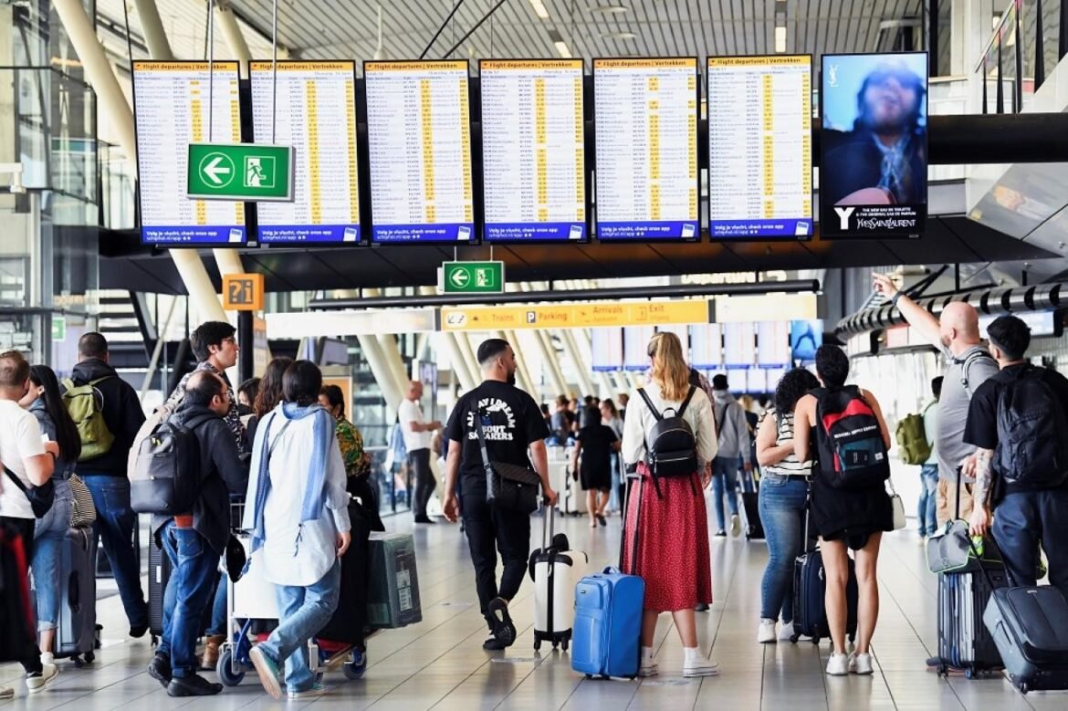 Busy airport terminal with passengers and rolling suitcases under large flight departure boards.