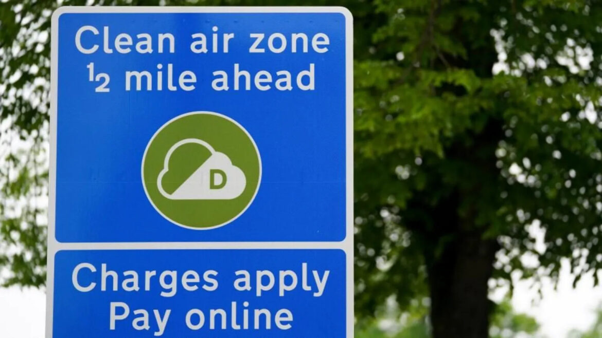 Blue road sign reading 'Clean air zone 1/2 mile ahead' with a green circular icon of a cloud, and a lower panel 'Charges apply Pay online'.