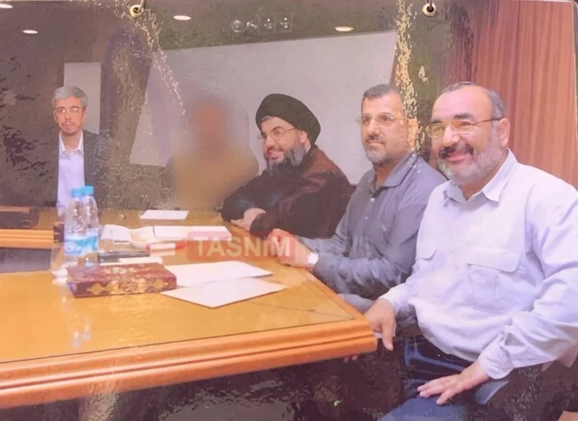 Four men sit at a conference table with papers; one man wearing a turban smiles at the camera.