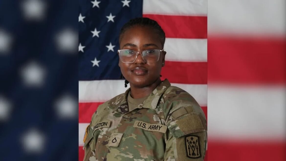 Person in U.S. Army camouflage uniform posing in front of a large American flag backdrop.