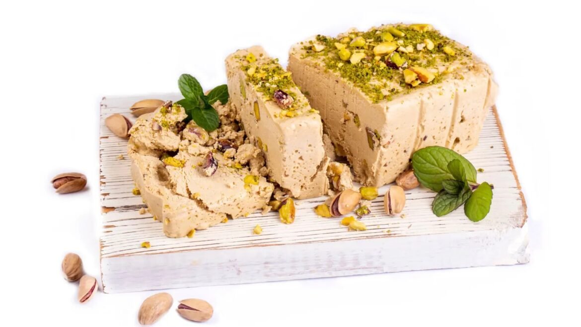 Slices of pistachio nougat on a rustic white board, garnished with chopped pistachios and fresh mint.