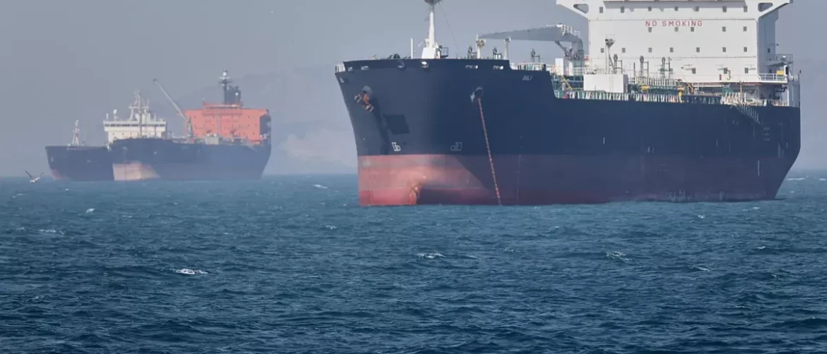 Two large cargo ships sail on blue sea, one in the foreground with a dark hull and red waterline.