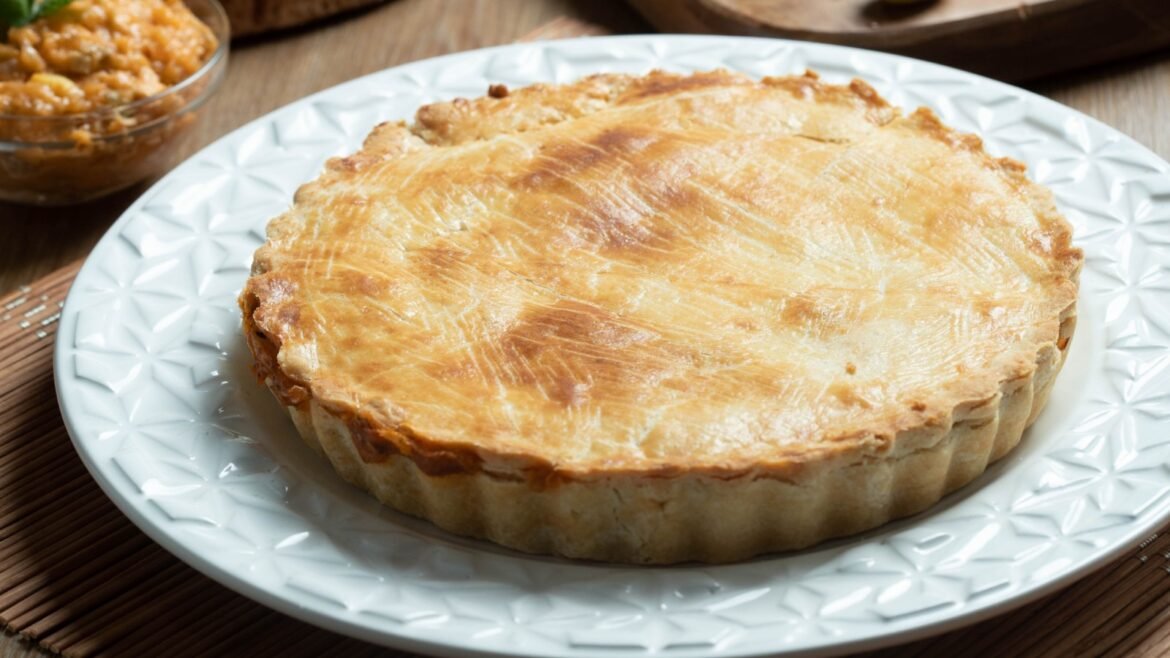 A golden-brown pie with a flaky crust on a decorative white plate, ready to serve at a table.