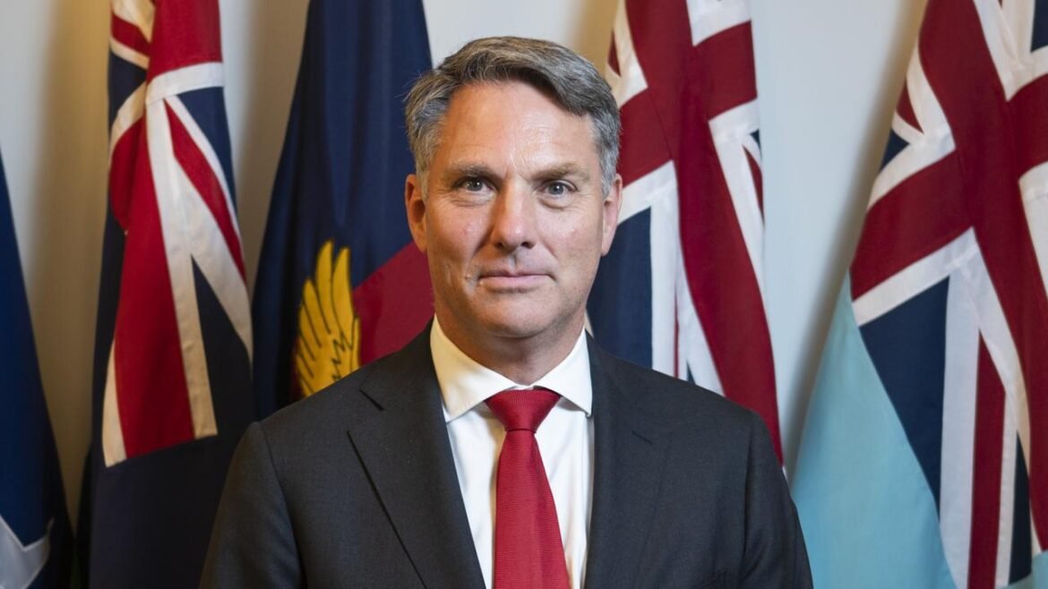 Professional man in a dark suit and red tie standing in front of multiple national flags.