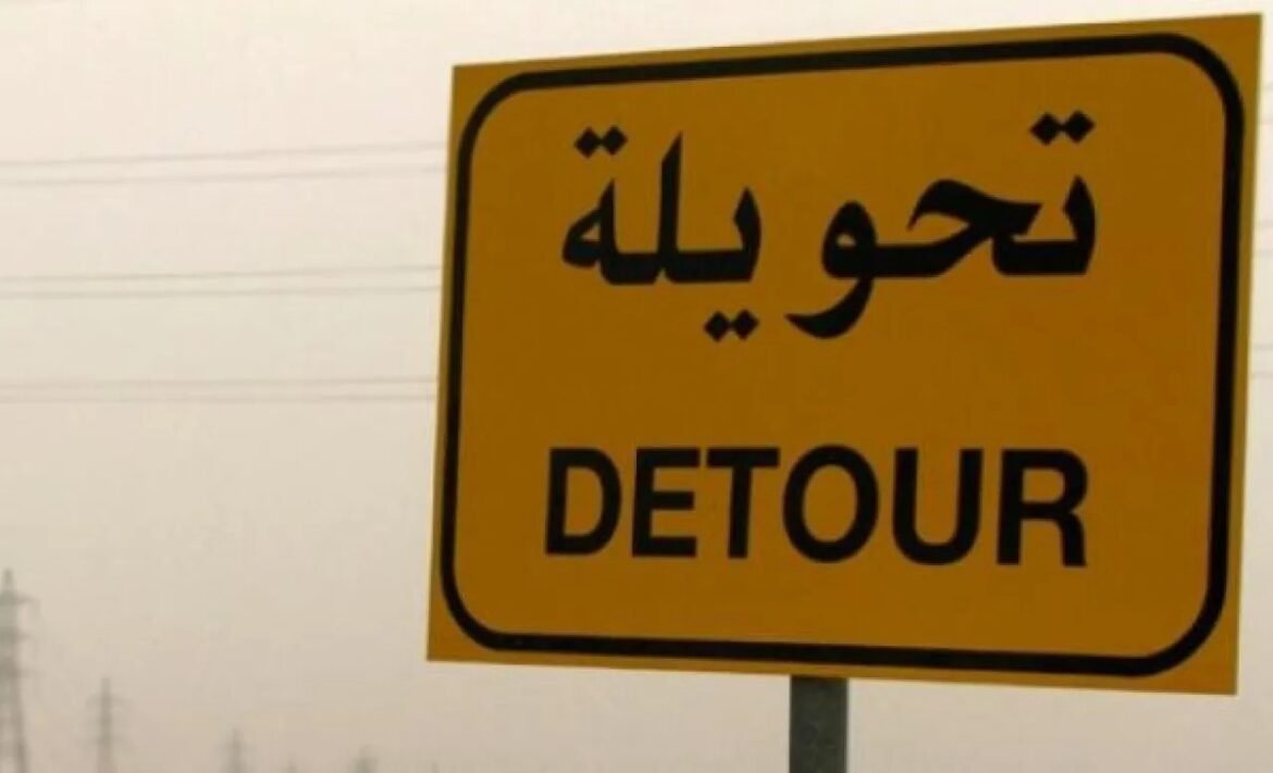 Yellow detour road sign with Arabic text and the word DETOUR in English on a pole.