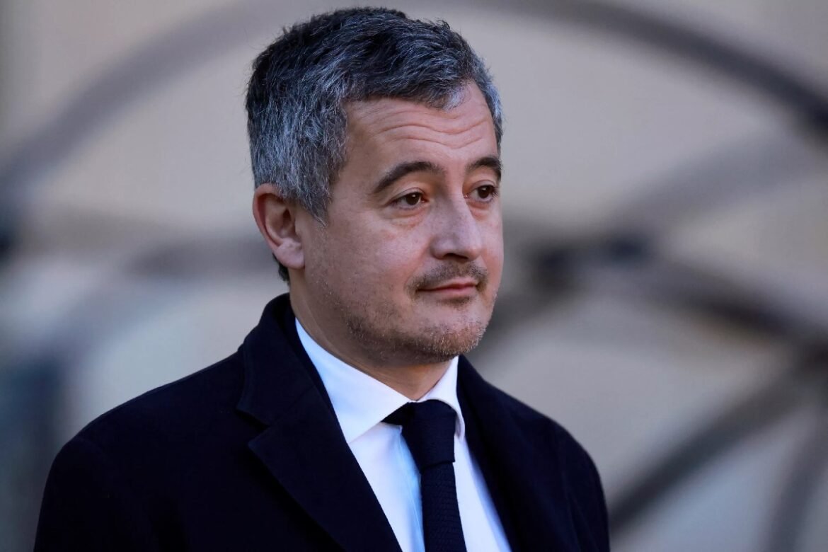 Man in a dark suit and tie standing outdoors, looking to the right with a neutral expression.