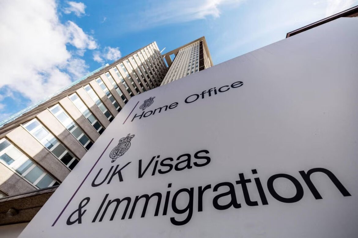Sign on a government building reading Home Office UK Visas & Immigration with a modern tower in the background against a blue sky.
