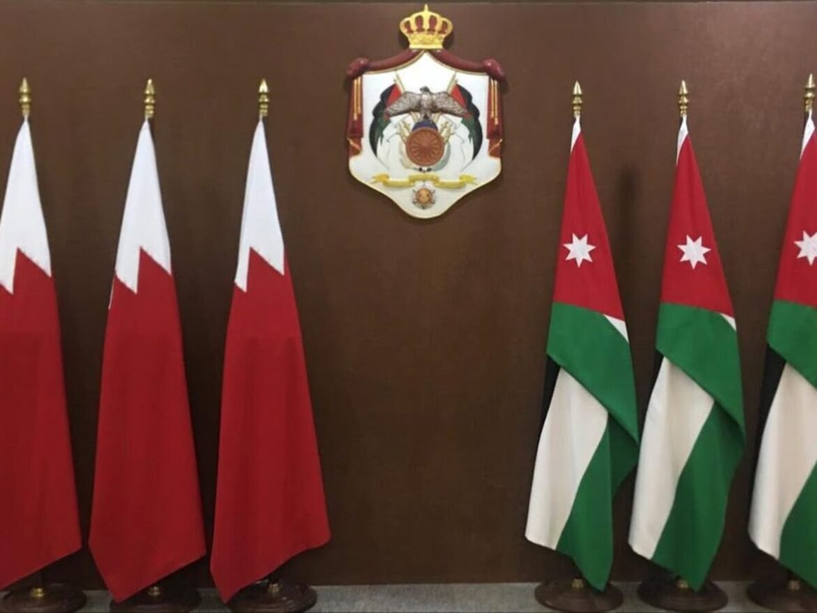 Row of red-and-white flags on the left and Jordanian flags on the right, with a crest and crown on a brown wall in the center.