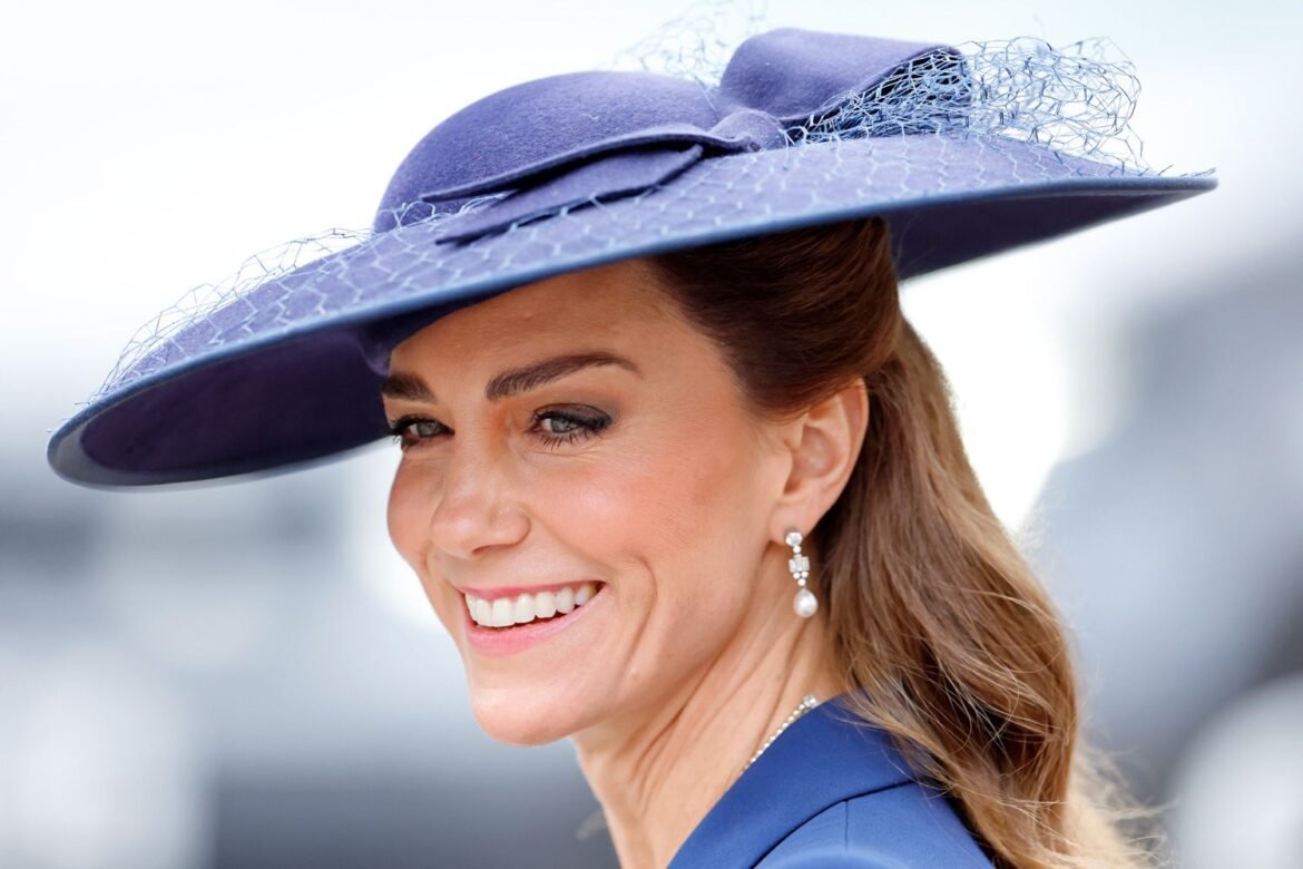 Smiling woman in a blue wide-brim hat with veil netting, dressed in blue, outdoors.