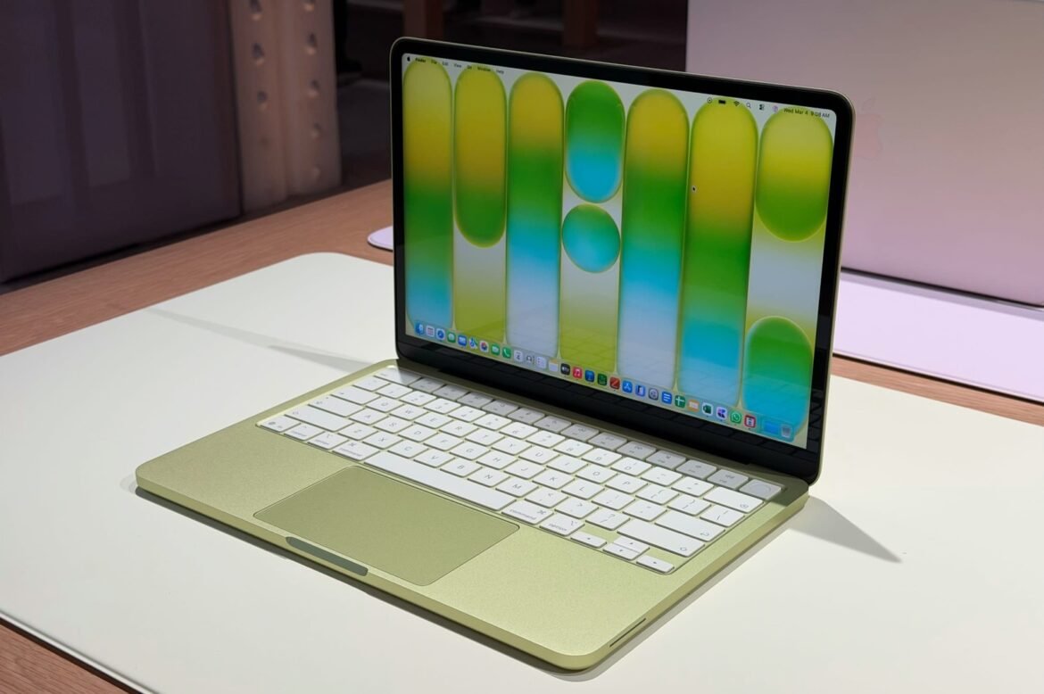 Gold laptop with white keyboard open on a white table, displaying a colorful wallpaper of green and yellow vertical shapes on the screen.