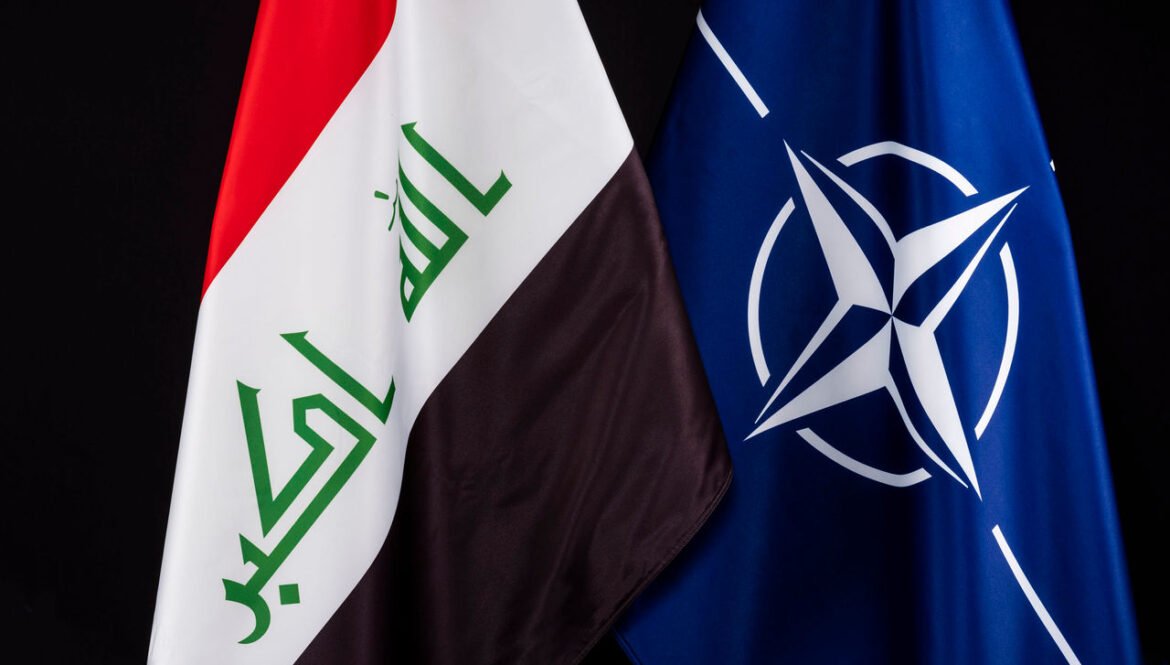 Two flags draped together: the Iraqi flag on the left and the blue NATO flag on the right against a black background, signaling international cooperation.