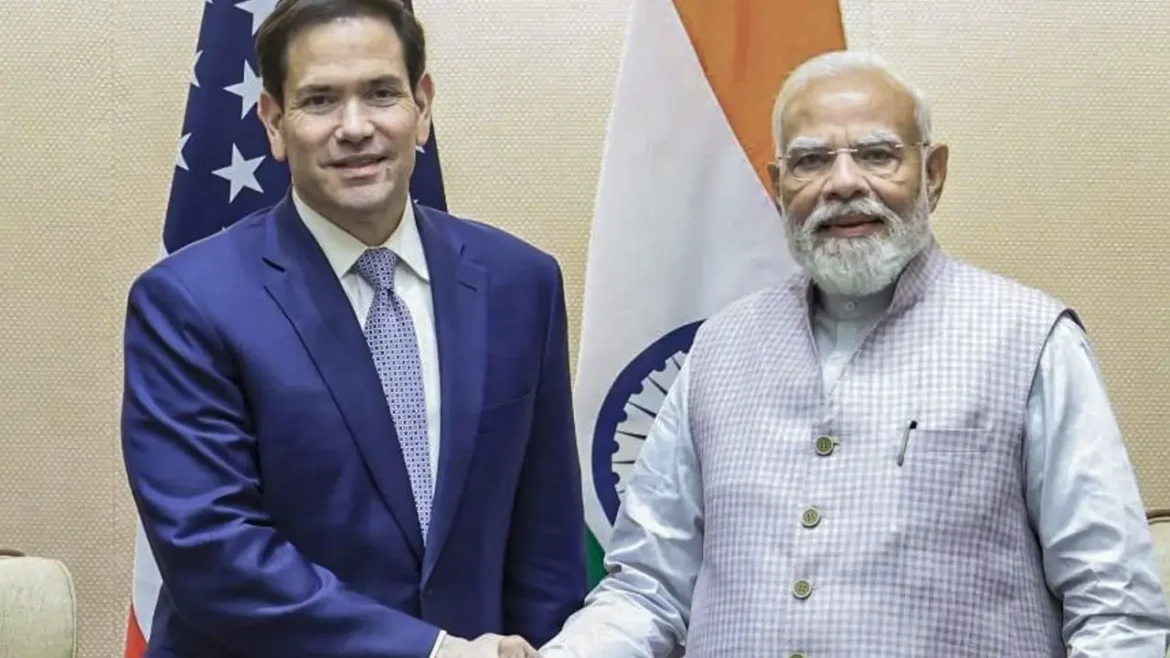 Two men in business attire shake hands in front of US and India flags, signaling a formal meeting or agreement.