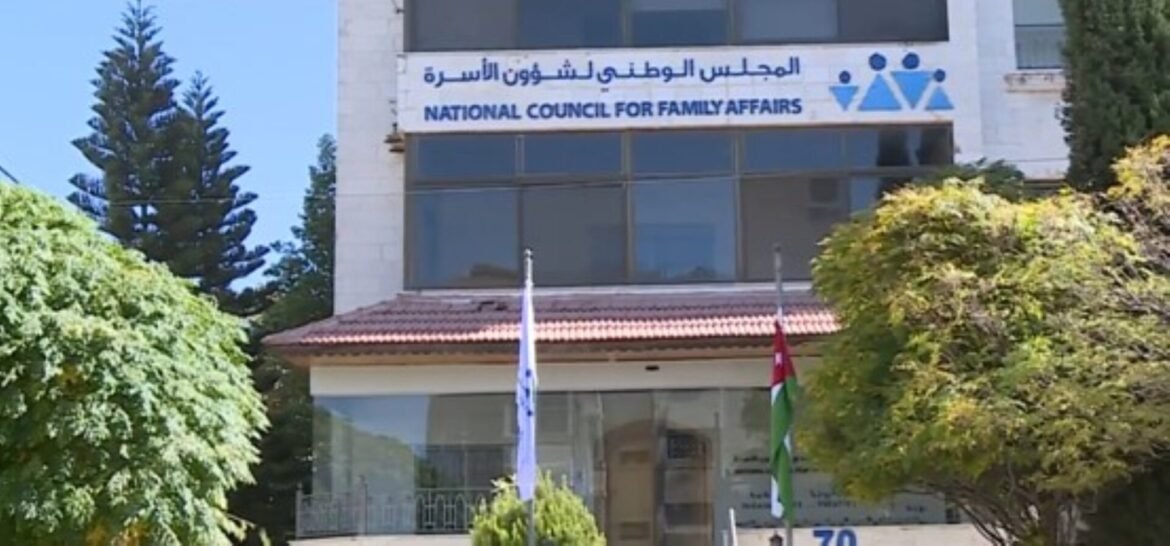 Front of a government building with a sign reading 'National Council for Family Affairs' in English and Arabic, with two flagpoles and surrounding trees.