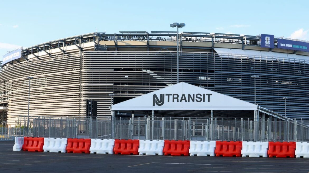 NJ Transit tent set up in front of a large stadium with red-and-white barriers surrounding the area behind a chain-link fence.