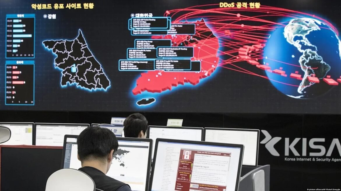 Office control room with several people at desks viewing computer monitors; a large digital dashboard on the wall shows a map of Korea and a globe with red network lines, labeled DDoS data, and the KISA logo.