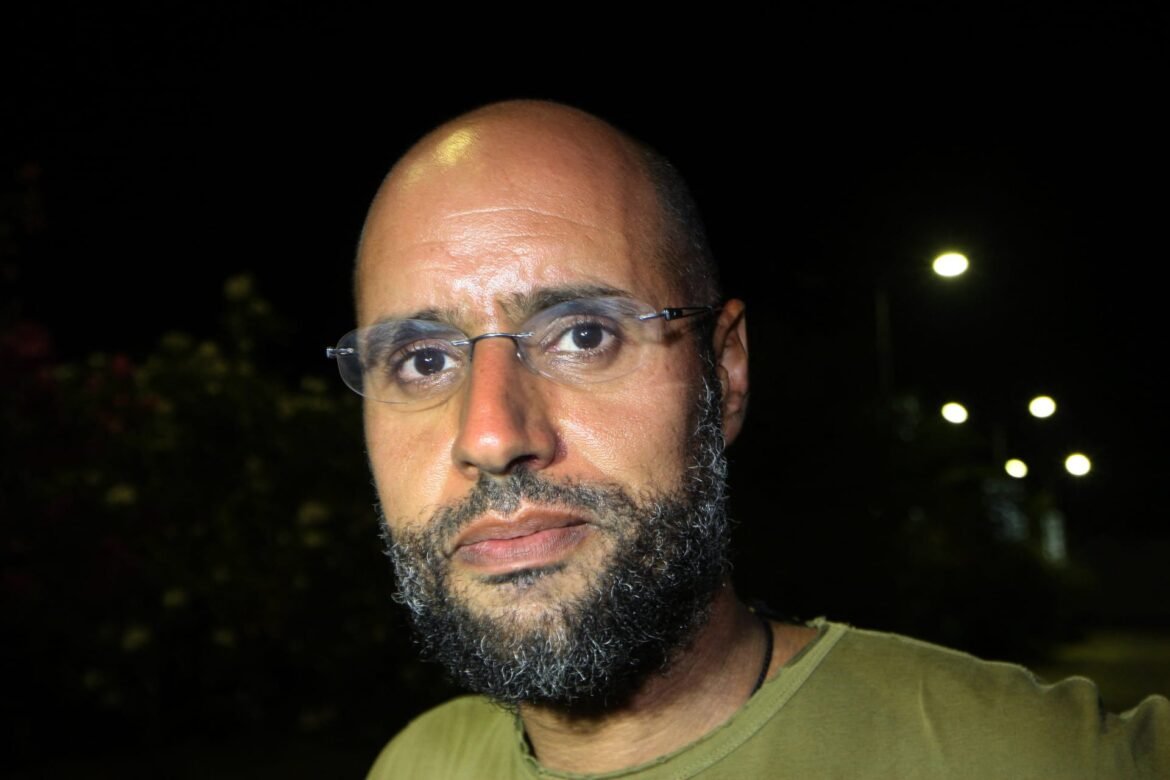Close-up portrait of a bearded man with glasses at night, with blurred streetlights in the background.