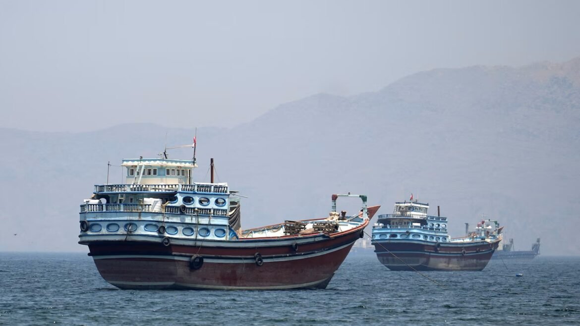 Large blue and white passenger boat anchored in calm sea with two smaller boats in the background and hazy mountains on the horizon