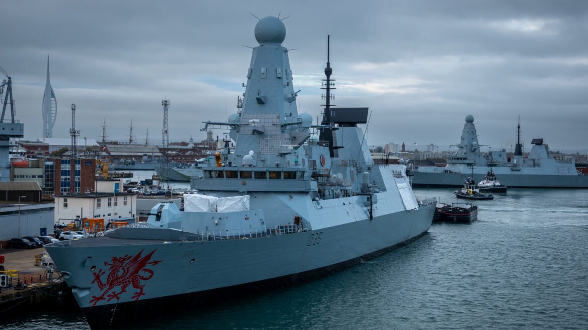 Large gray naval destroyer docked at a port, with a red dragon emblem on the bow and the hull number D35 visible.",