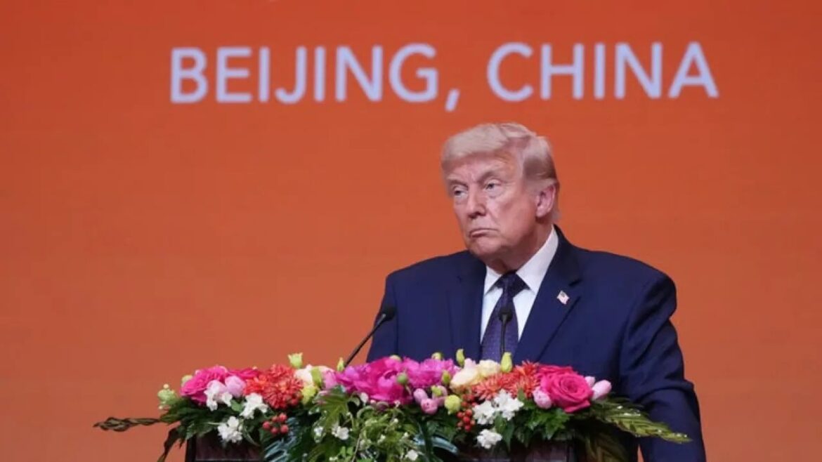 A man in a dark suit stands at a podium with a floral arrangement, an orange backdrop reading 'BEIJING, CHINA'.