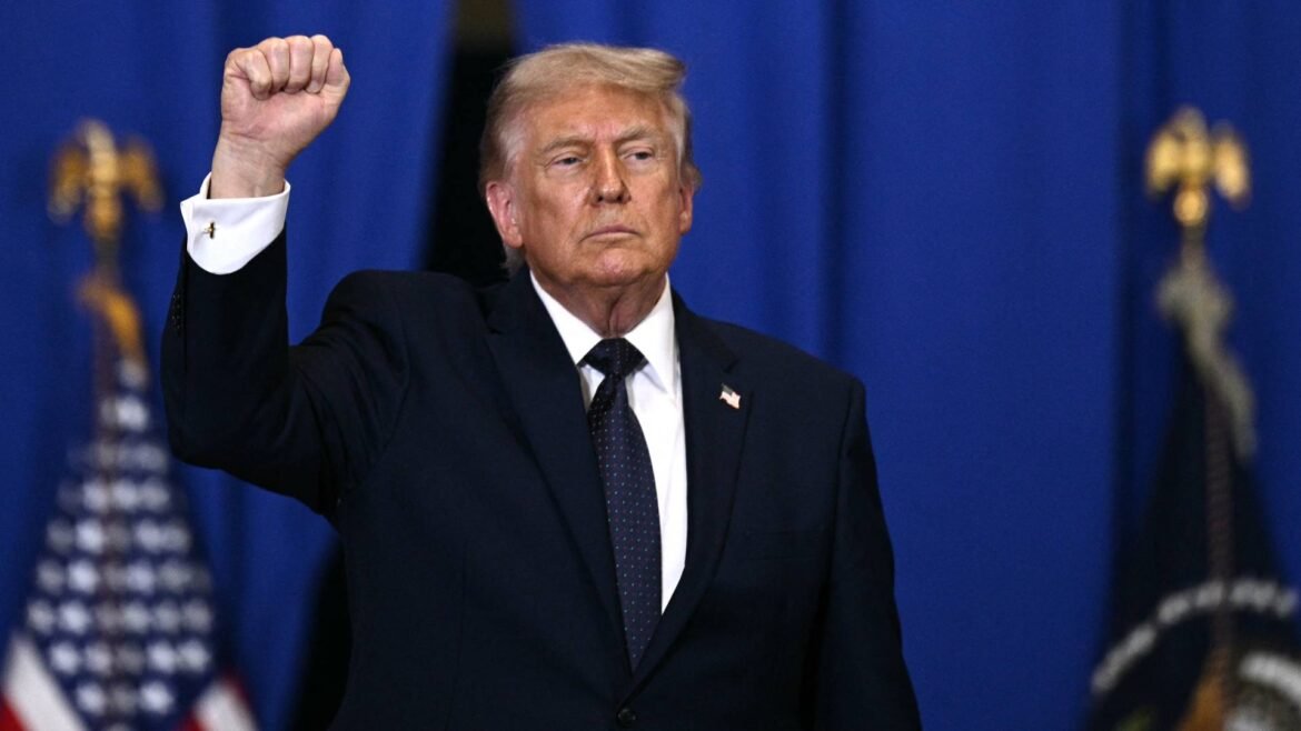 Former U.S. president Donald Trump raises his right fist on stage, against a blue backdrop.