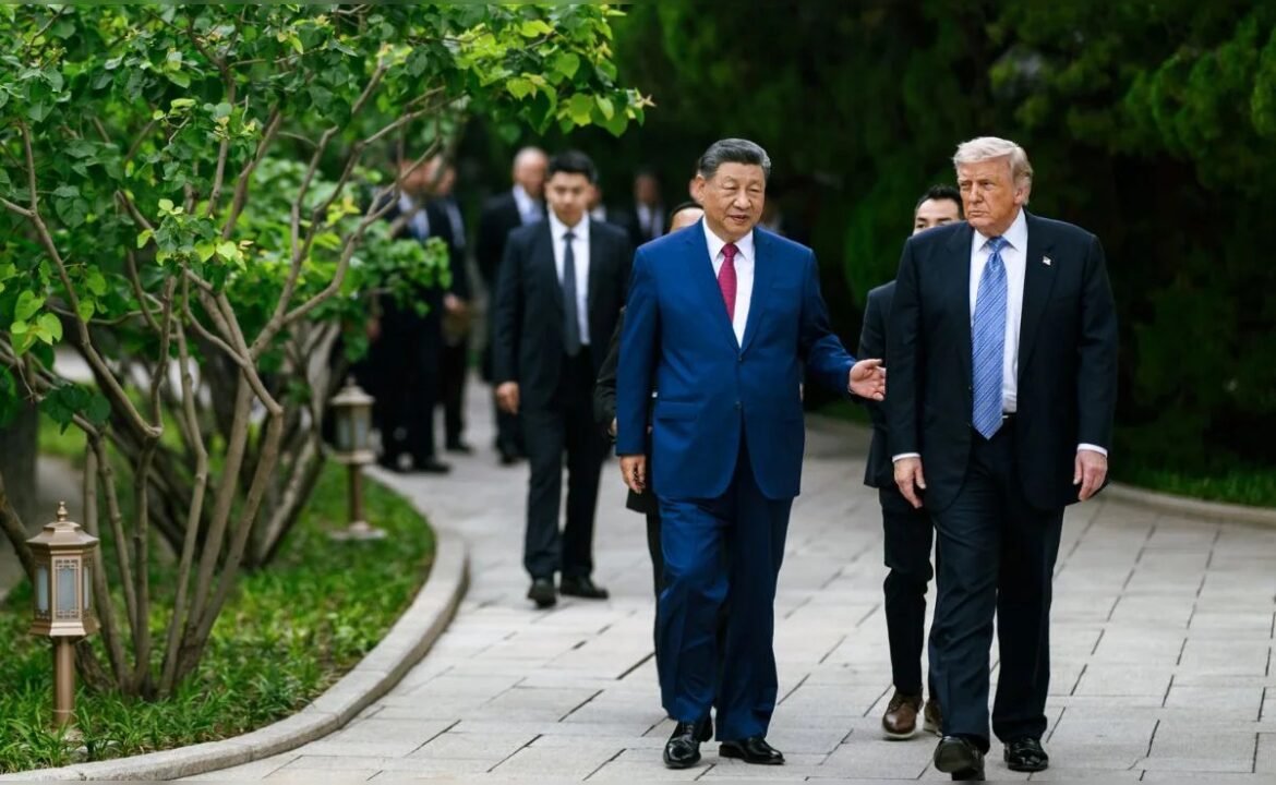 Chinese President Xi Jinping in a blue suit with red tie walks beside former U.S. President Donald Trump along a stone garden path, aide group in the background.