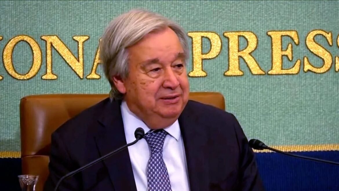 Older man in a dark suit speaks at a press conference, microphone in front of him.