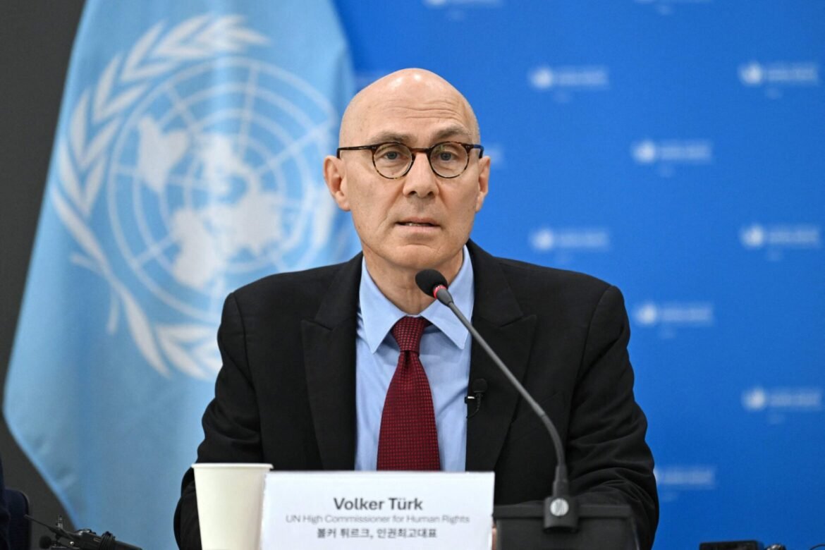 Man with glasses and a red tie speaking at a UN podium, banner backdrop with the UN emblem behind him (Volker Türk).