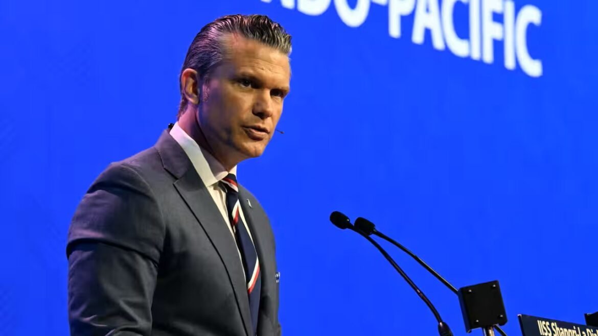 Male speaker in a gray suit and striped tie delivers a speech at a podium on a blue stage backdrop.
