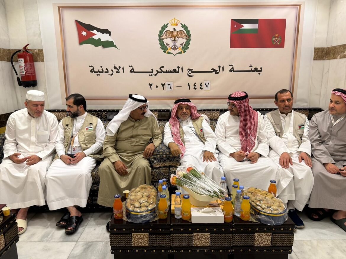 Group of men in traditional white robes seated on a couch in a formal room, with a banner and Jordanian flags behind them.