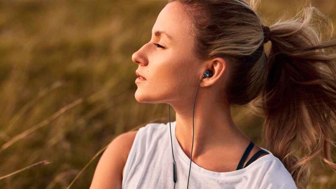 Woman with eyes closed wearing wired earbuds outdoors at sunset, enjoying music.