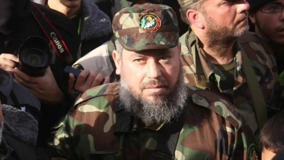 Bearded man in camouflage uniform and cap with insignia, surrounded by photographers and fellow soldiers.