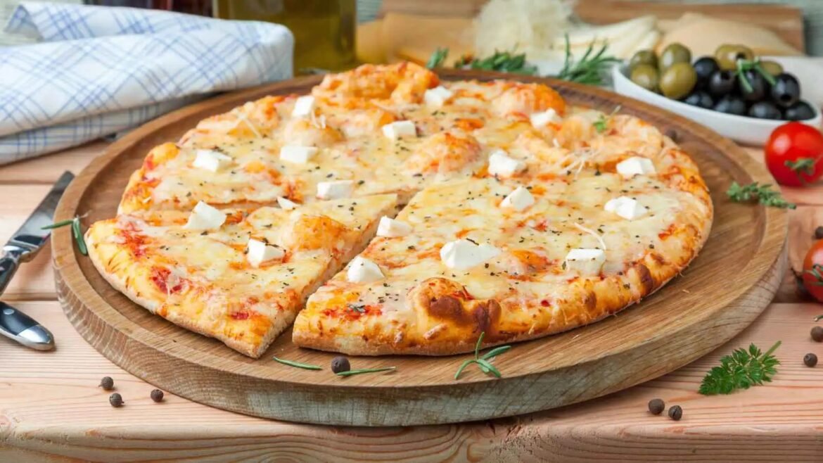 Cheese pizza cut into slices, arranged on a round wooden board with a few herbs nearby.